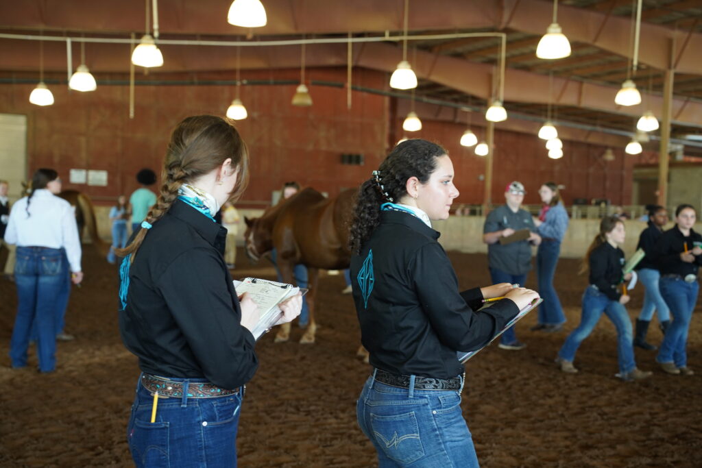 Two female 4-H'ers standing with clipboards in a barn during Horse Judging.