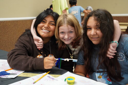 Three youth sitting at a table posing with a toothbrush and pipe cleaners.