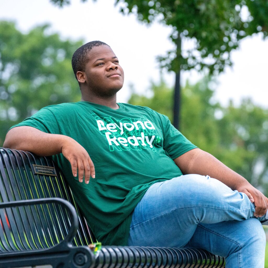 A 4-H'er sitting on a bench wearing a green t-shirt with 'Beyond Ready' text