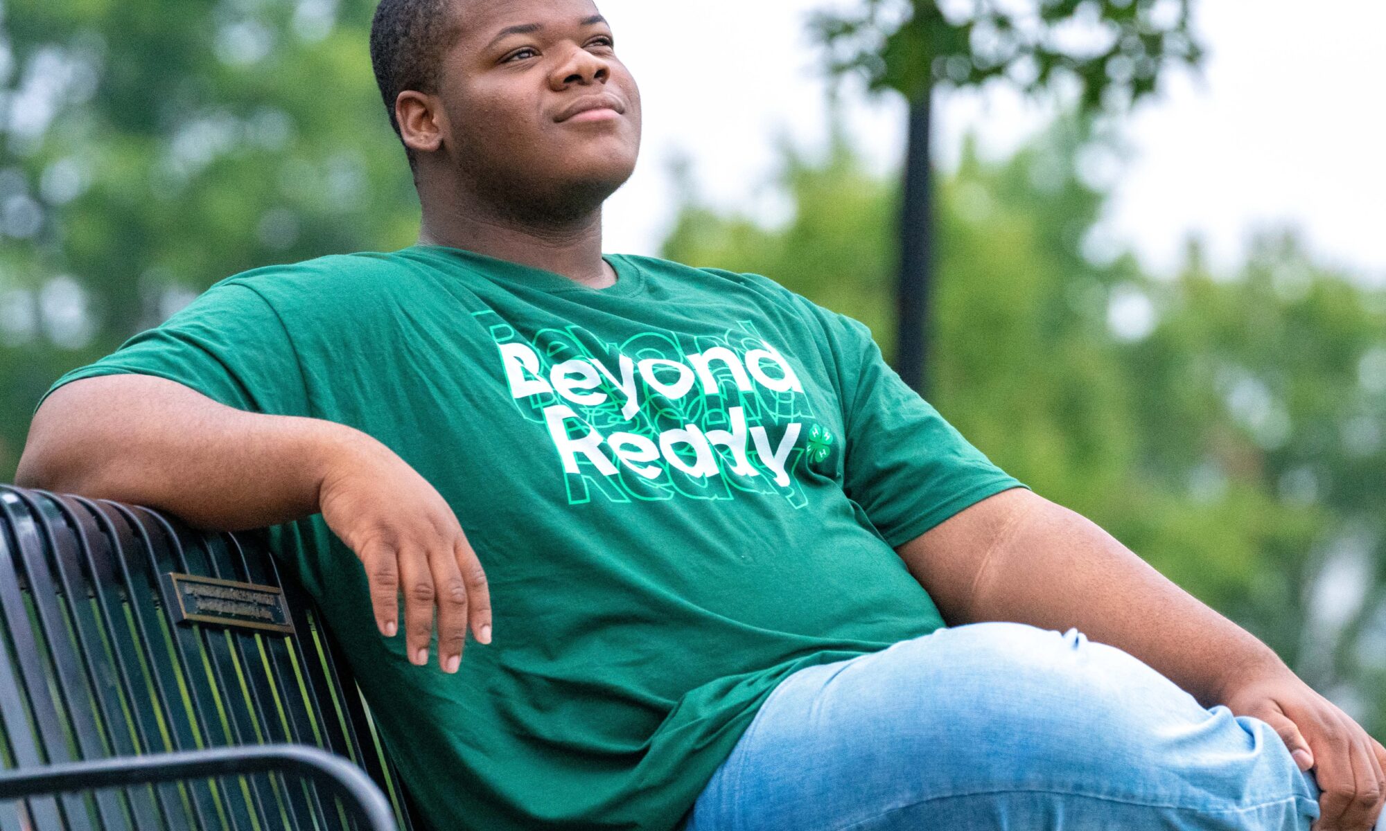 A 4-H'er sitting on a bench wearing a green t-shirt with 'Beyond Ready' text