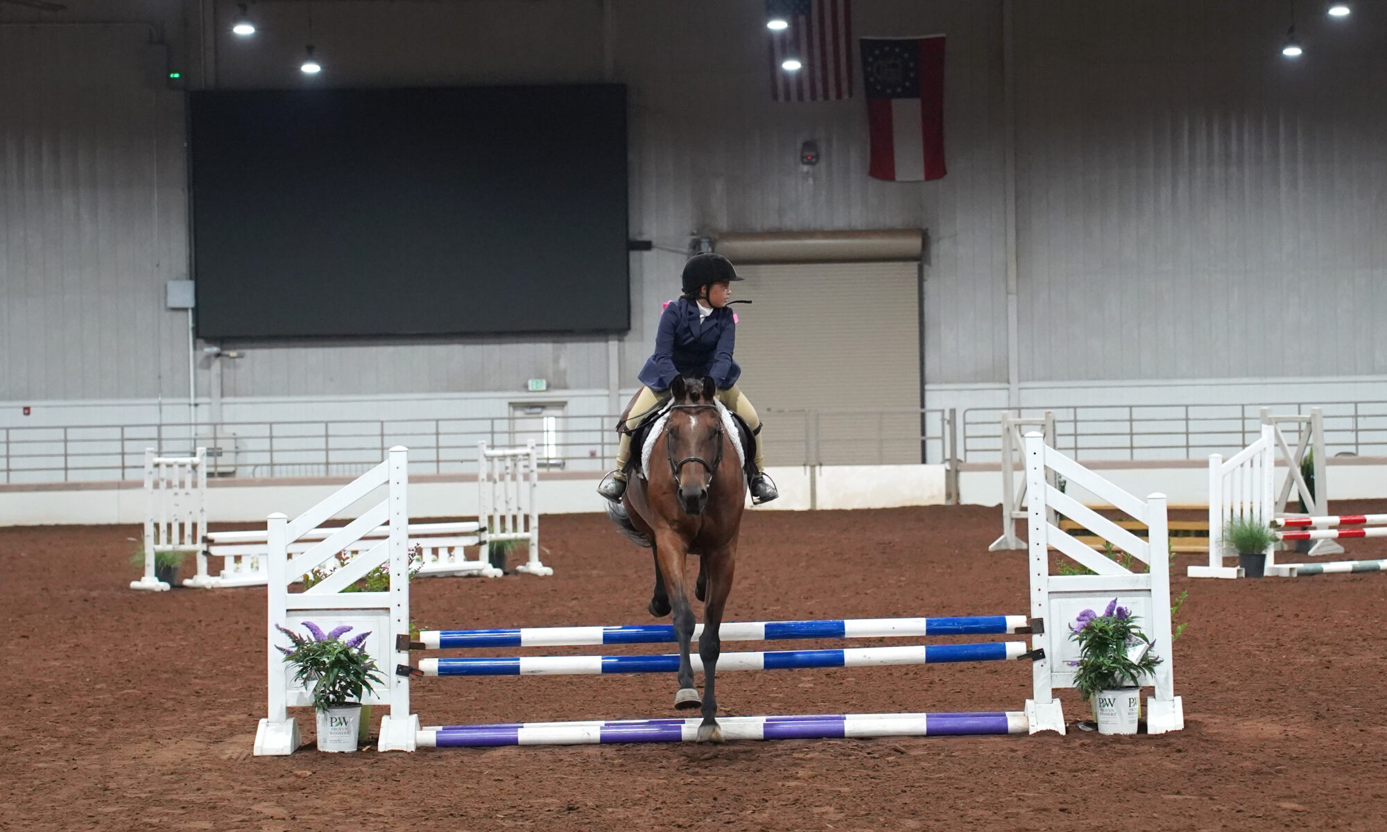 A female student riding a horse and jumping over a small fence
