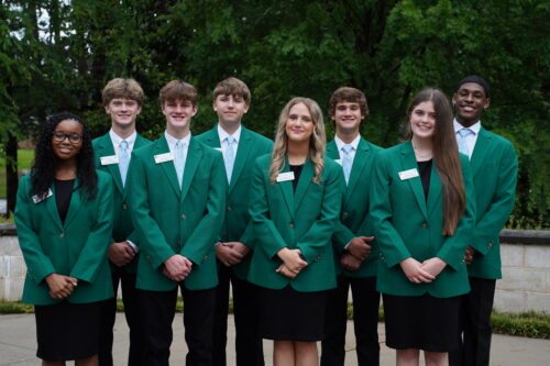 A group of eight students posing dressed in green blazers