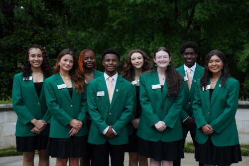 A group of eight students posing dressed in green blazers