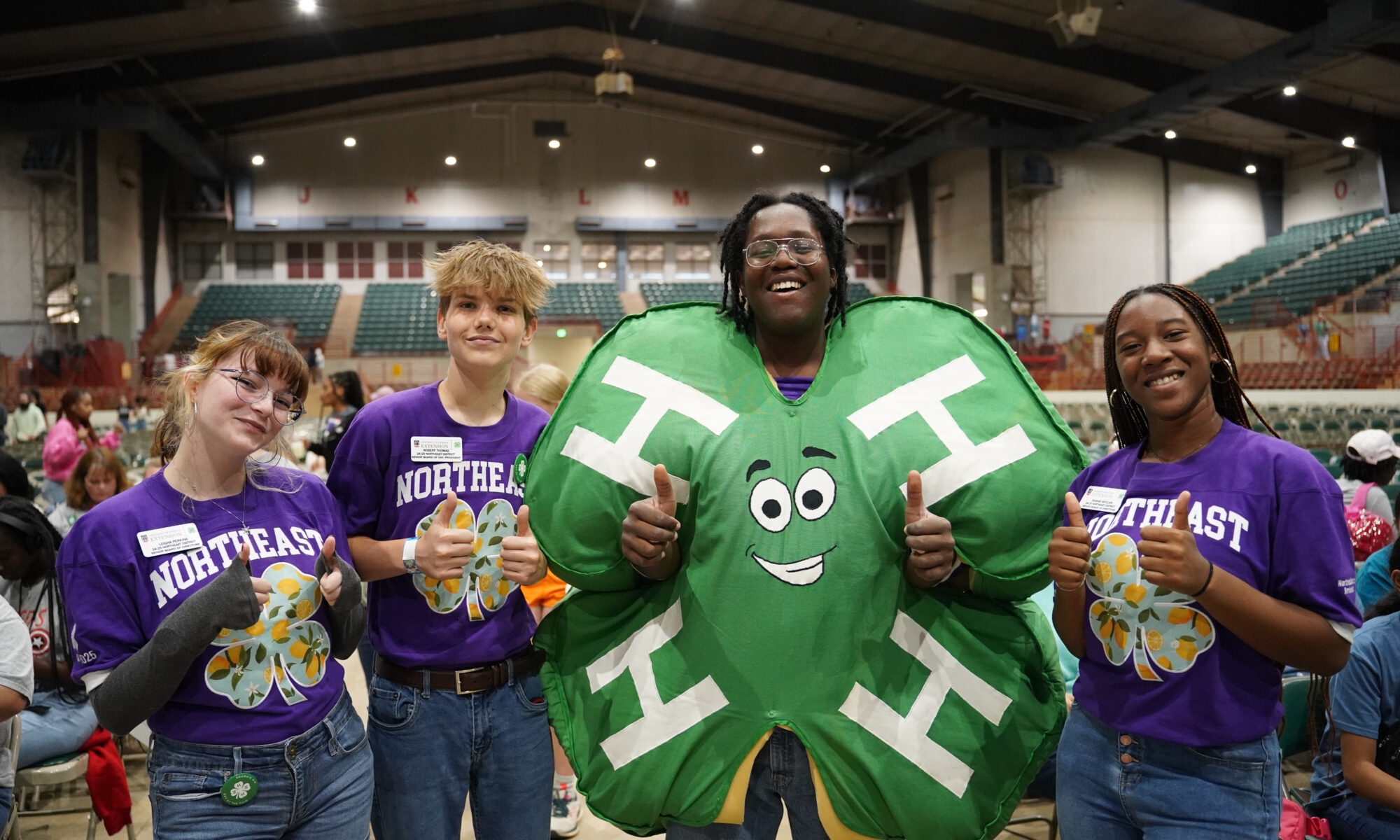 Three youth wearing purple 4-H jerseys pose with a fourth individual wearing a clover costume