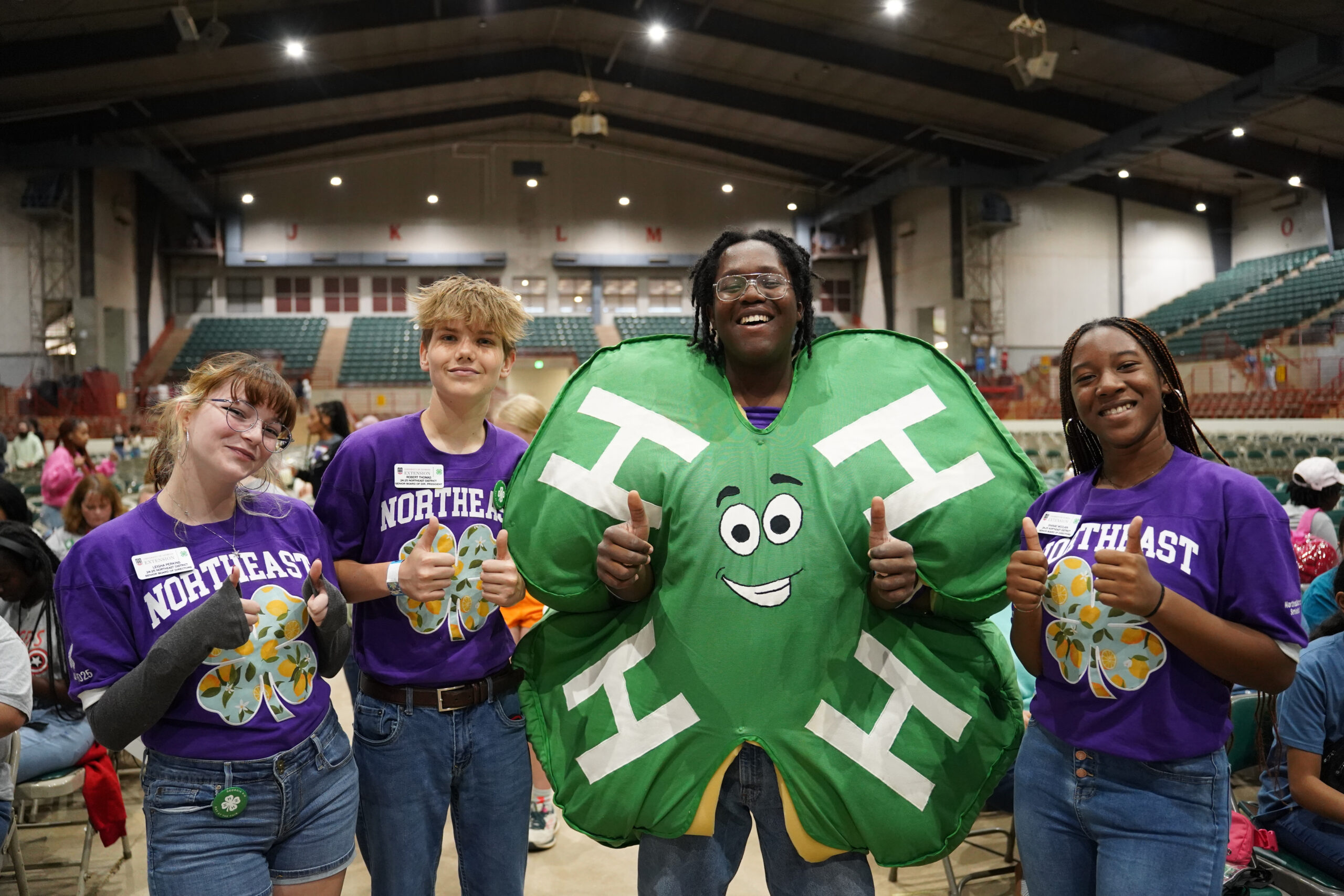 Three youth wearing purple 4-H jerseys pose with a fourth individual wearing a clover costume