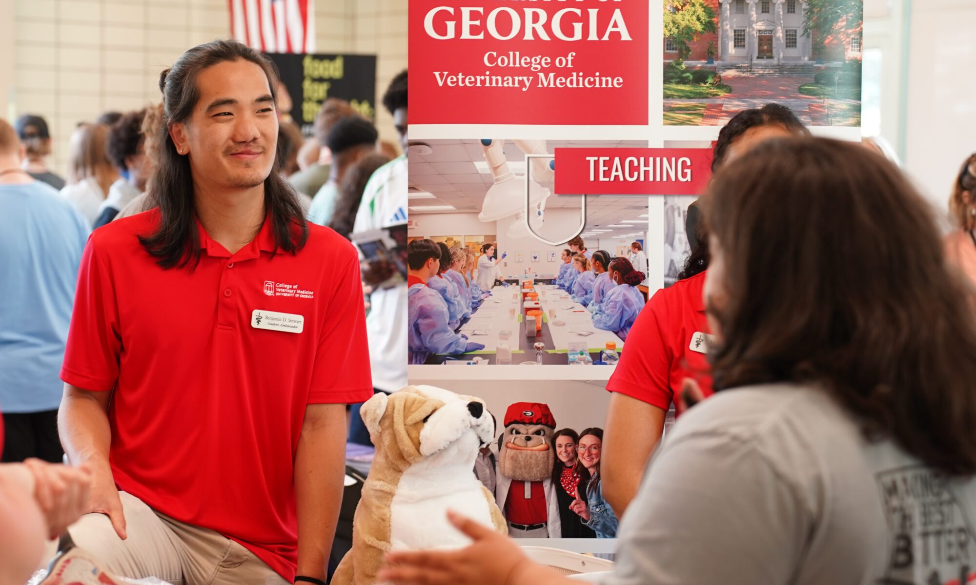 A UGA employee wearing a red polo standing behind an information table at a college resource fair.