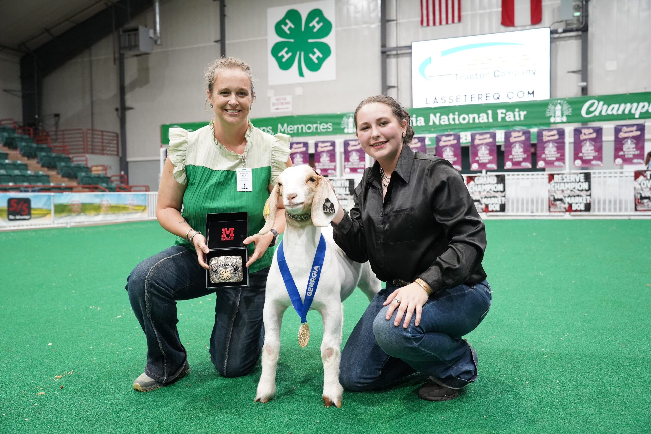 An adult and a youth posing with a sheep wearing a medal in the livestock ring
