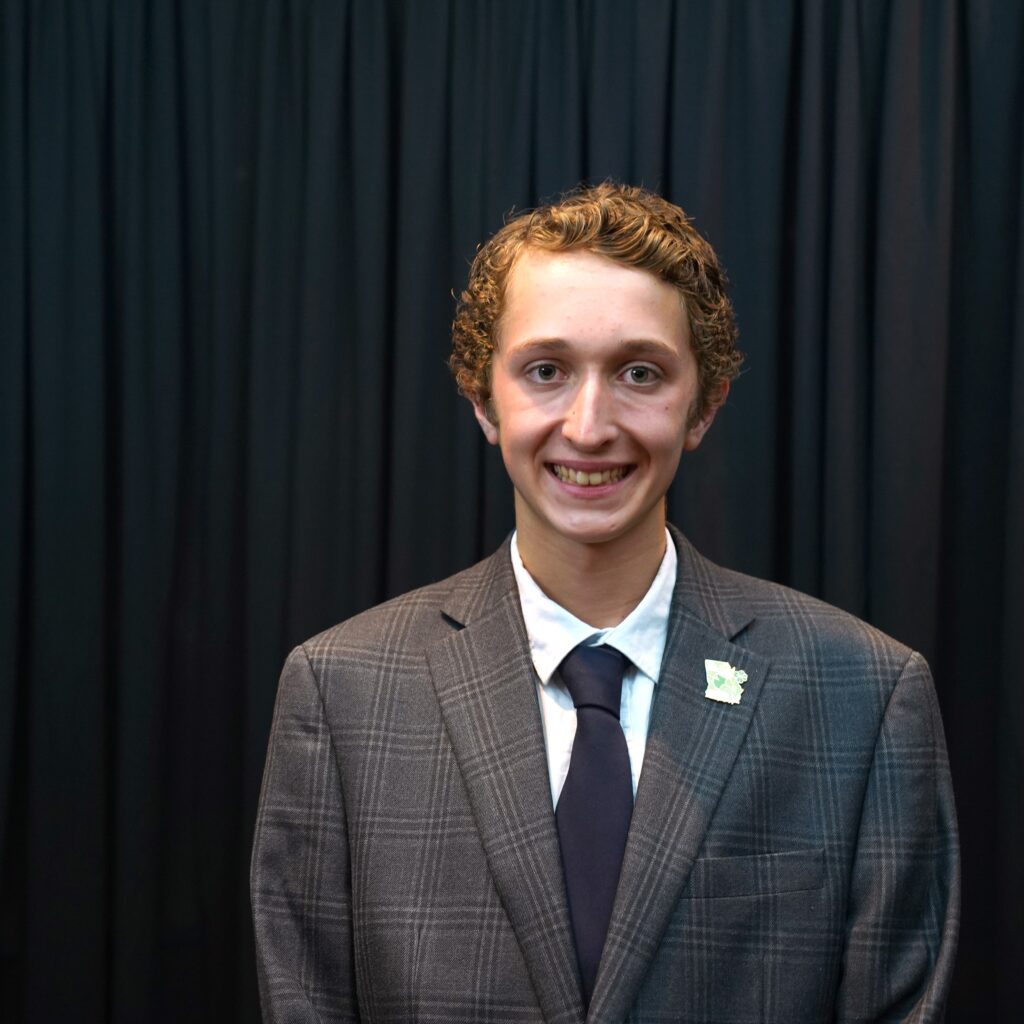 a 4-H'er wearing a grey suit smiling against a black backdrop