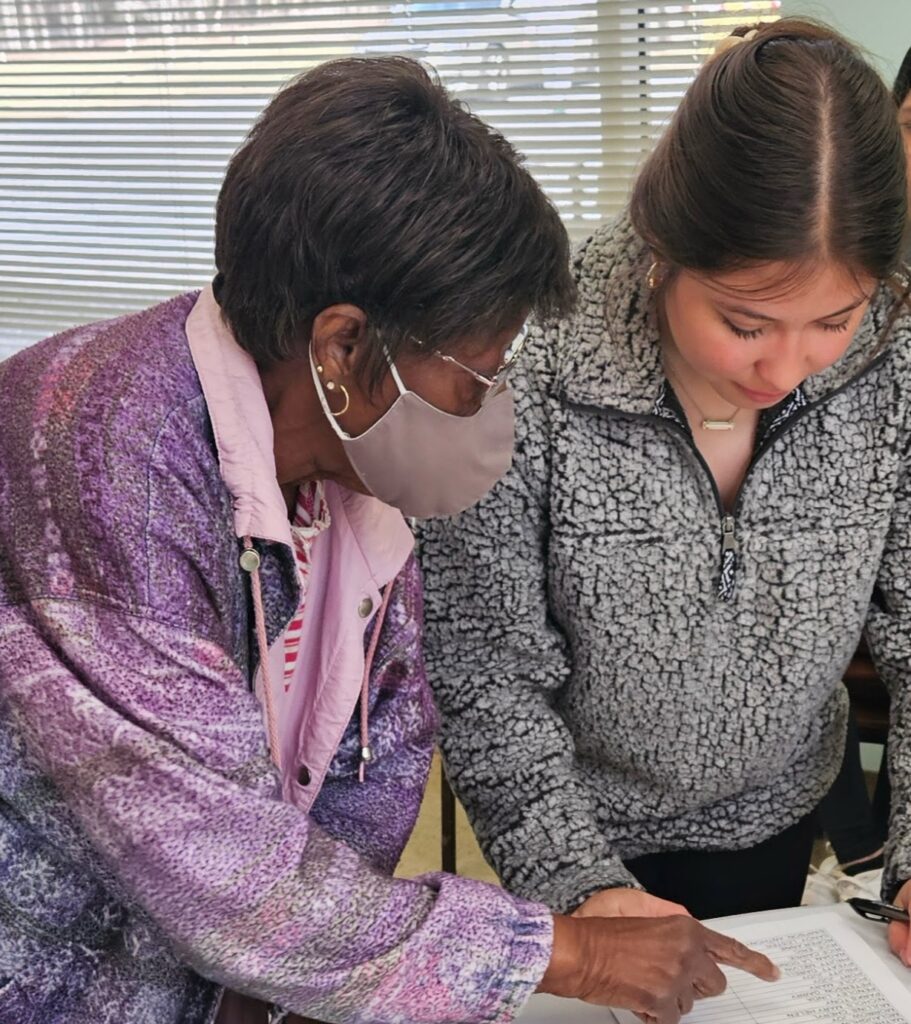 A student assisting a senior citizen with a craft project
